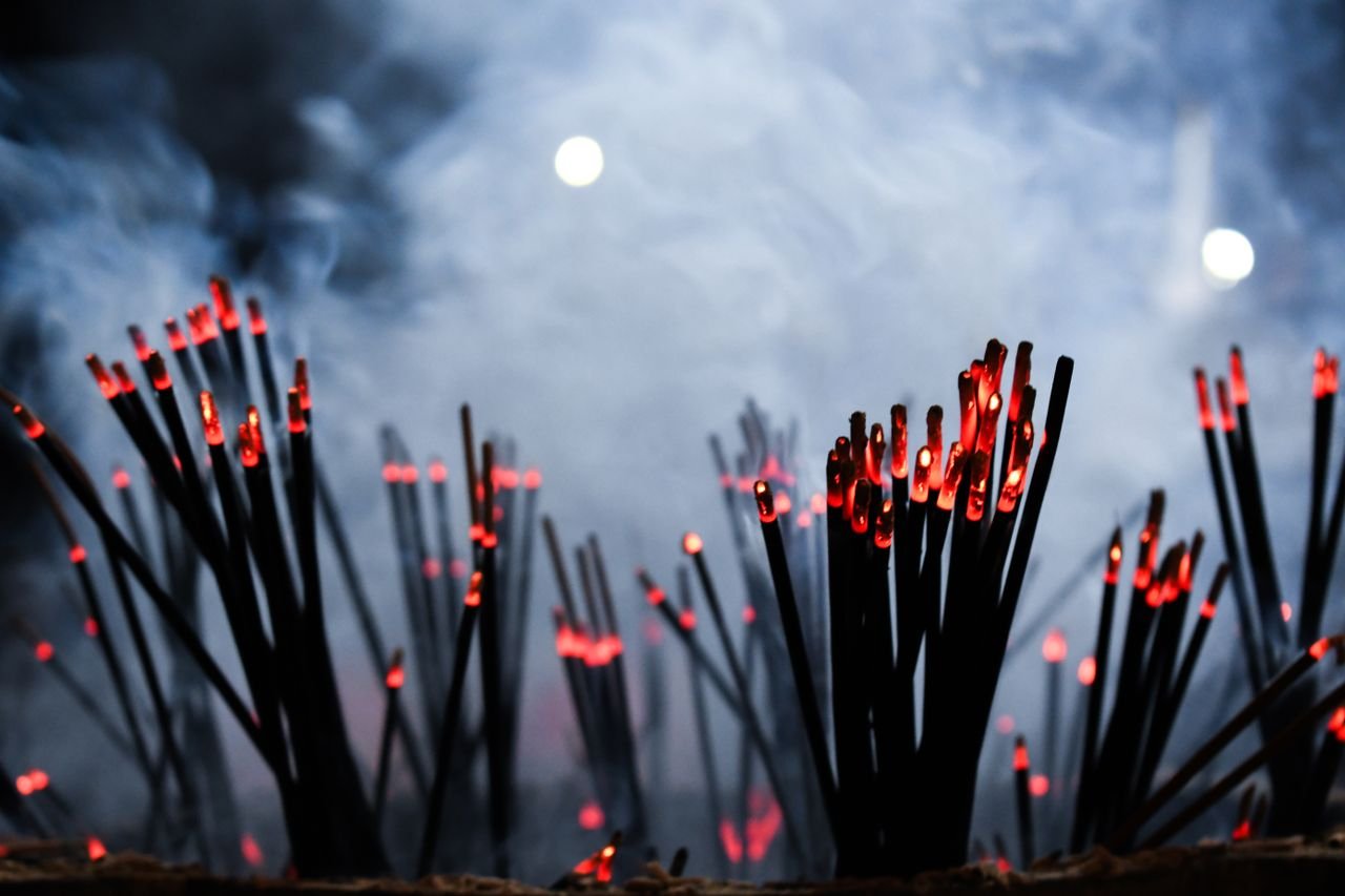 A striking silhouette of aromatic incense sticks with glowing embers against a smoky background.