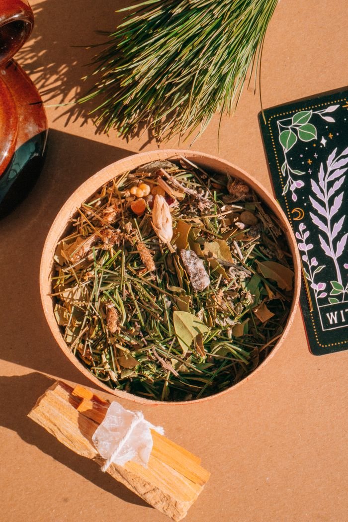 Top view of mixed dry herbs in a wooden bowl with tarot card and Palo Santo.