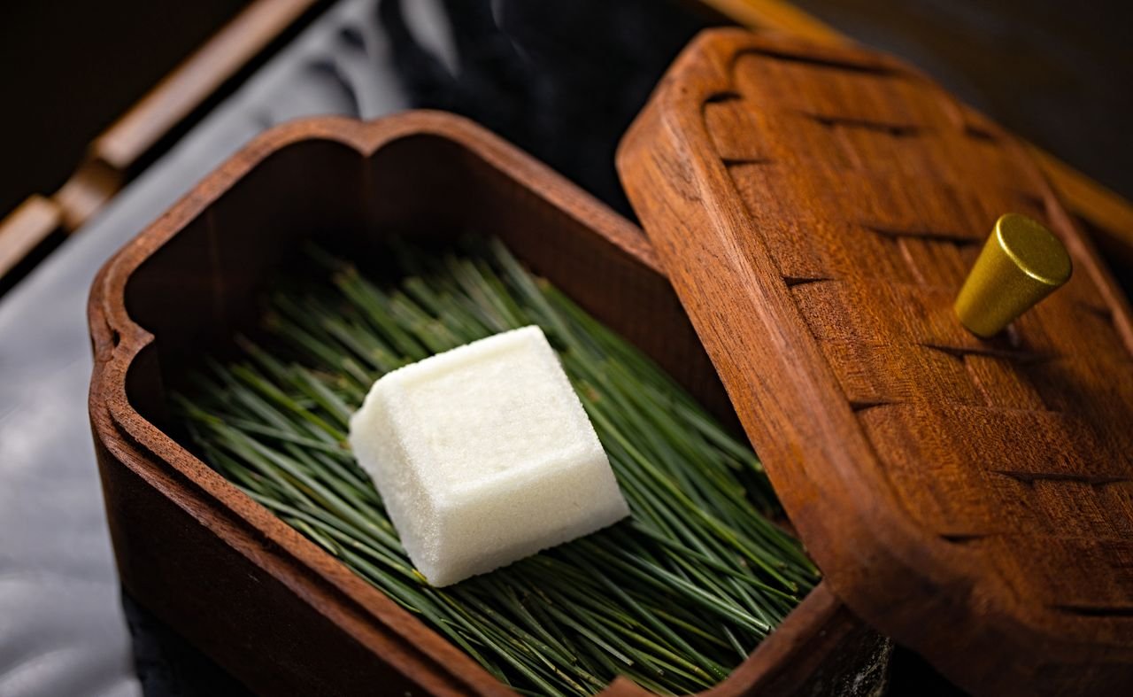Close-up of a white soap bar resting on pine needles inside a wooden box.